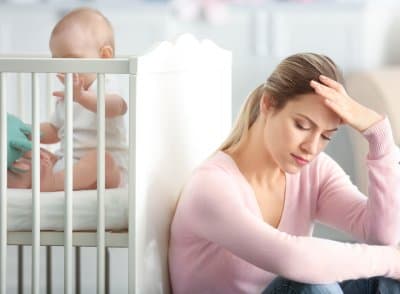 Müde Mutter sitzt erschöpft am Bett ihres Babys